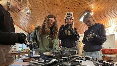 Vier jungen Menschen hinter einem Berg alter Handys