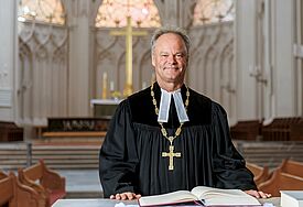 Bischof Jeremias trägt einen Talar und steht am Altar im Greifswalder Dom St. Nikolai