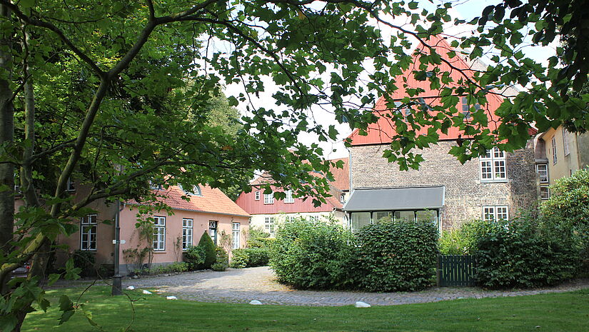Blick durch den Park des St. Johannisklosters mit seinem Baumbestand auf alte Gebäude mit roten Dächern