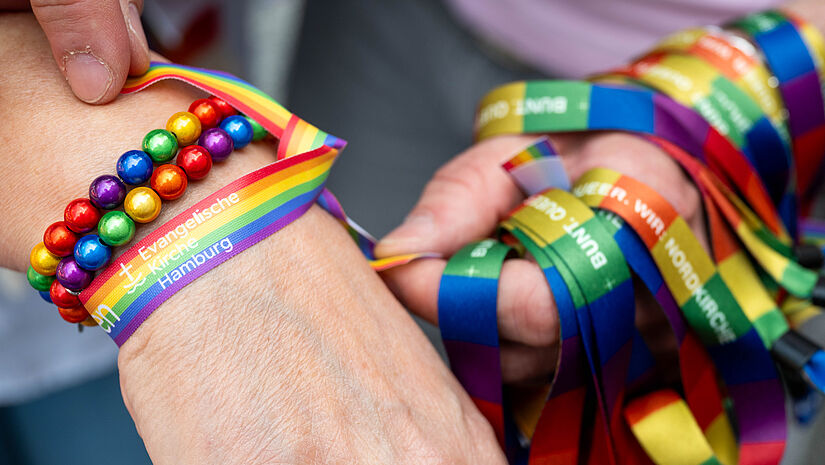Zwei Hände mit Segensbändern in Regenbogenfarben