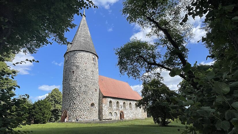 Der Blick auf eine Kirche aus Feldsteine. Links der dicke, runde Turm