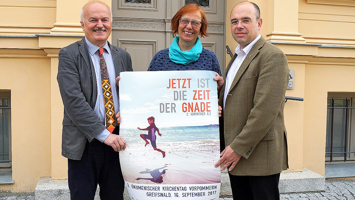 Referentin Barbara Schlicht, Ökumenepastor Matthias Tuve (li.) und Frank Hoffmann, Propst der katholischen Kirche in Vorpommern, präsentieren das Plakatmotiv des 3. Ökumenischen Kirchentags 2017