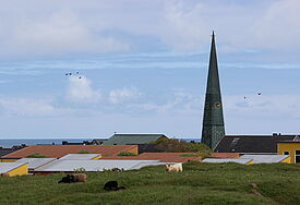 Die Kirchturmspitze der St.-Nicolai-Kirche auf der Norseeinsel Helgoland überragt die Dächer der Häuser im Ort.