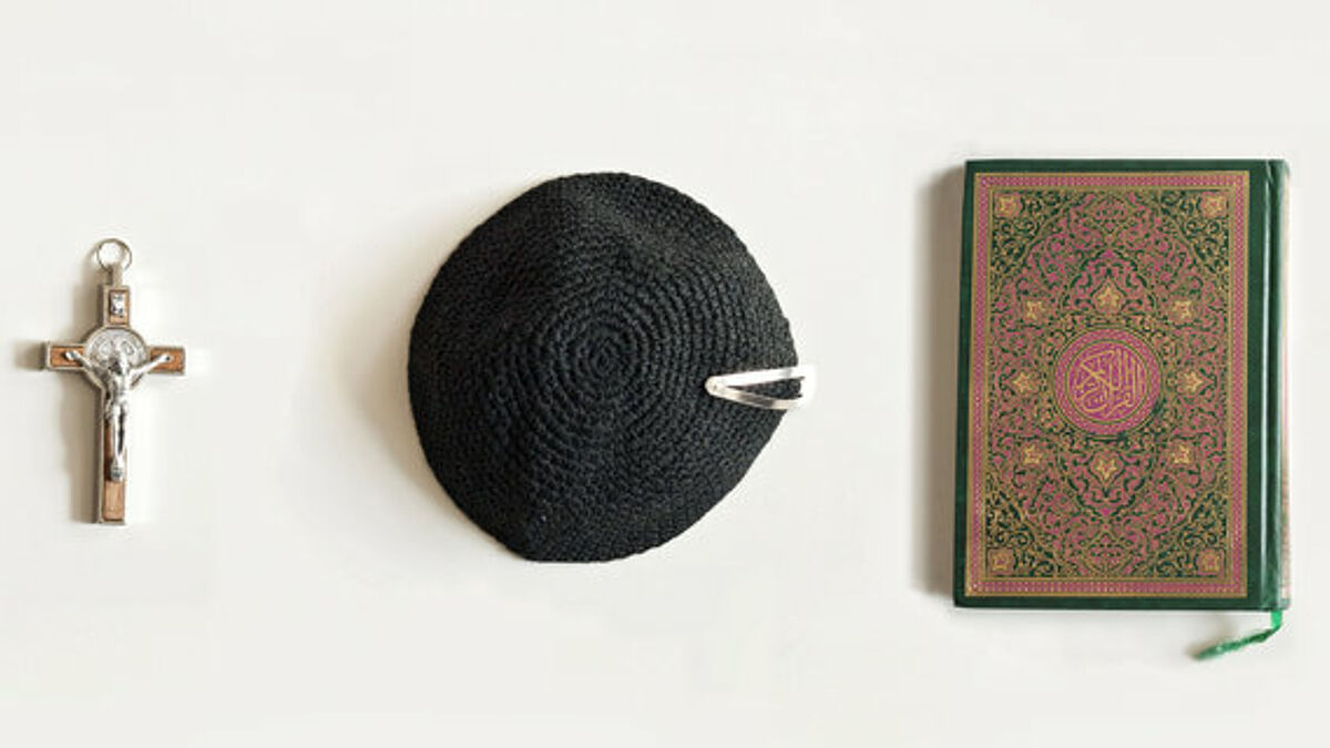 Symbole für die drei monotheistischen Weltreligionen Christentum, Judentum und Islam: Kreuz, Kipa und Koran