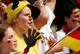 Fußballfans mit Hüten, Flaggen und Winkelementen fiebern mit