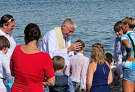 Täuflinge stehen knietief im Ostseewasser. In der Mitte Propst Sönke Funck im weißen Talar.