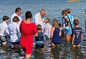 Täuflinge stehen knietief im Ostseewasser. In der Mitte Propst Sönke Funck im weißen Talar.