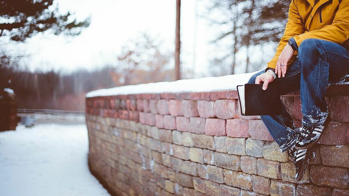 Mann sitzt mit Bibel auf Mauer