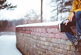 Mann sitzt mit Bibel auf Mauer