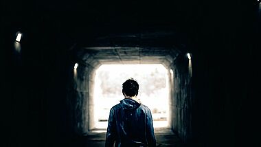 Mann steht mit dem Rücken zur Kamera in einem Tunnel, an dessen Ende Licht ist