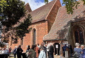 Beginn von Dorfkirche Mon Amour in Kirch Mummendorf: Menschen stehen im Frühsommer vor der Backsteinkirche