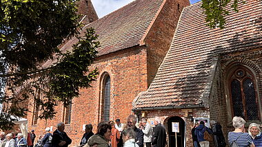 Beginn von Dorfkirche Mon Amour in Kirch Mummendorf: Menschen stehen im Frühsommer vor der Backsteinkirche