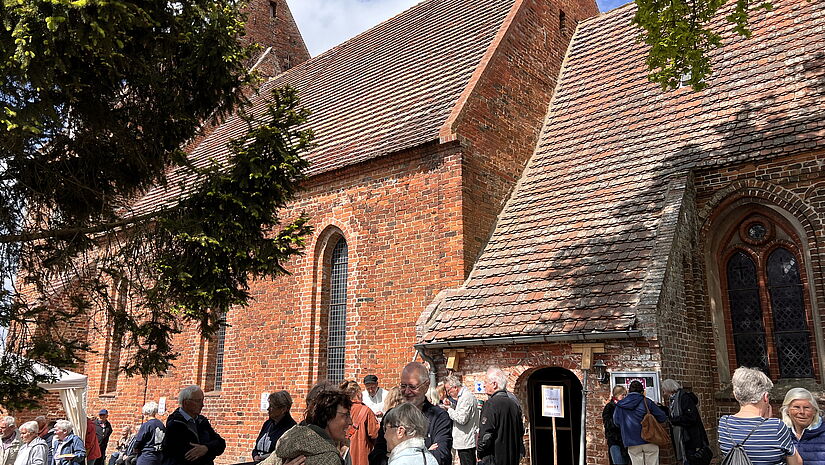 Beginn von Dorfkirche Mon Amour in Kirch Mummendorf: Menschen stehen im Frühsommer vor der Backsteinkirche