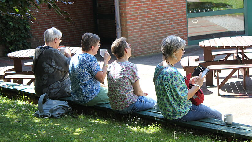 Vier Frauen sitzen im Schatten auf einer Rasenkante
