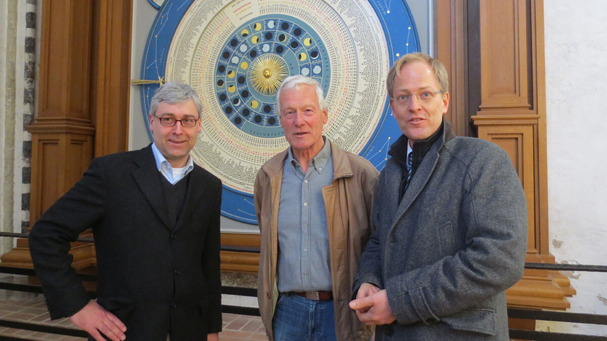 Sie funkelt, strahlt und tickt im Takt: Projektleiter Justus Deecke (v.li), Jochen Otto sen. und Pastor Robert Pfeifer stehen vor der frisch sanierten Astronomischen Uhr von St. Marien.