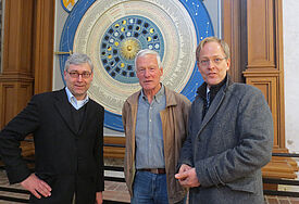Sie funkelt, strahlt und tickt im Takt: Projektleiter Justus Deecke (v.li), Jochen Otto sen. und Pastor Robert Pfeifer stehen vor der frisch sanierten Astronomischen Uhr von St. Marien.