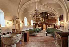 Innenraum der Kirche mit Rundbögen und einem Taufbecken