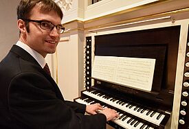 Mann in schwarzem Pullover schaut in die Kamera und spielt dabei auf den Tasten der neuen Orgel