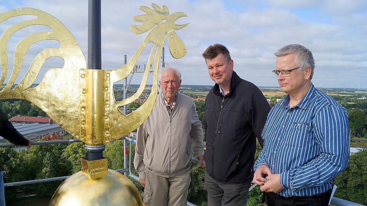 Über den Dächern der Hansestadt (v.r.n.l.): Pastor Michael Mahlburg, Architekt Ulf-Gernot Kirmis und Gunther Kirmis, früherer Leiter des Bauamts der pommerschen Kirche, während der Installation des Wetterhahns in einer Höhe von 53 Metern auf der Turmspitze der Greifswalder Jacobikirche. 