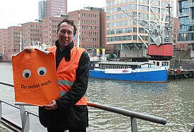 Propst Thomas Drope macht am Ersatz-Liegeplatz der Flussschifferkirche in der Hamburger Hafencity Werbung für die Tour zum "Kirchentag auf dem Weg"