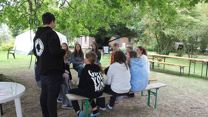 KonfiCamp Junge Menschen sitzen draußen in einer Gesprächsrunde unter einem Baum zusammen 