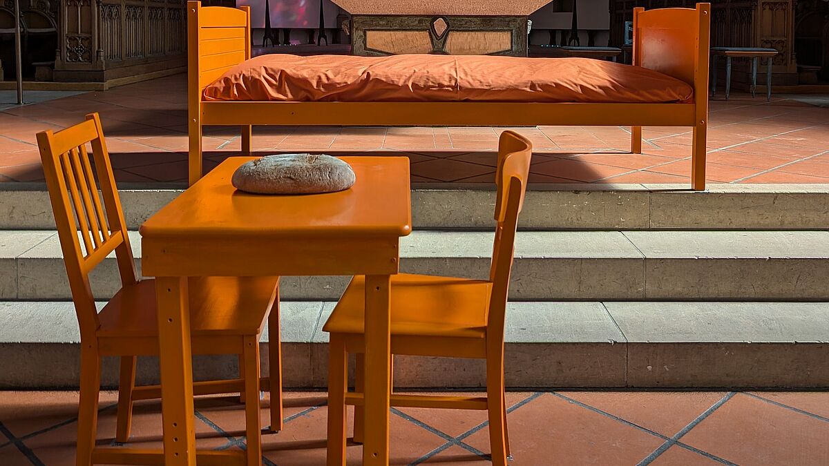 Bestandteil der Wanderausstellung „Zuflucht geben – gemeinsam hoffen“ ist eine Installation aus orangefarbenen Möbeln, die die Notwendigkeiten des Kirchenasyls bildlich und symbolisch darstellt: Ein Bett steht für einen geschützten Schlafplatz, Tisch, Stuhl und Brot verweisen auf Gemeinschaft, Beziehung und menschliche Nähe. 