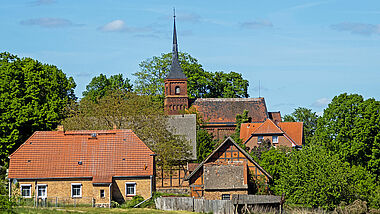Eine Kirche steht leicht erhöht im MIttelpunkt eines kleinen Dorfes.
