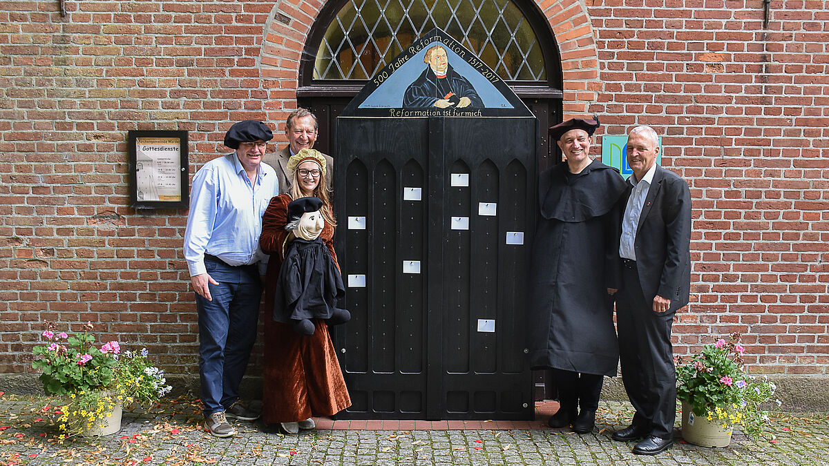 Pastor Roland Scheel (Kirchengemeinde Warder), Laura Grimm (als Katharina von Bora), Peter Wiegner (Präses der Kirchenkreissynode), Pastor Karsten Baden-Rühlmann (als Martin Luther, Bildungswerk) und Pastor Ekkehard Wulf (stv. Propst des Kirchenkreises Plön-Segeberg und Kirchengemeinde Nahe) an der Thesentür.