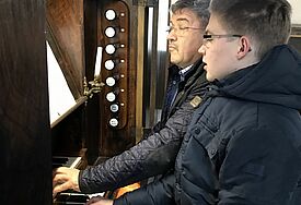 Zwei Männer sitzen in Daunenjacke an der Orgel
