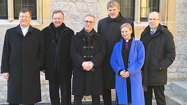 Bischöfe stehen alle in schwarz vor einem Gebäude, nur Bischöfin Fehrs trägt einen blauen Mantel