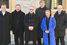 Bischöfe stehen alle in schwarz vor einem Gebäude, nur Bischöfin Fehrs trägt einen blauen Mantel