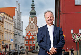 Bischof Jeremias steht im Anzug in Greifswald. Im Hintergrund. ist der Domturm zu erkennen.