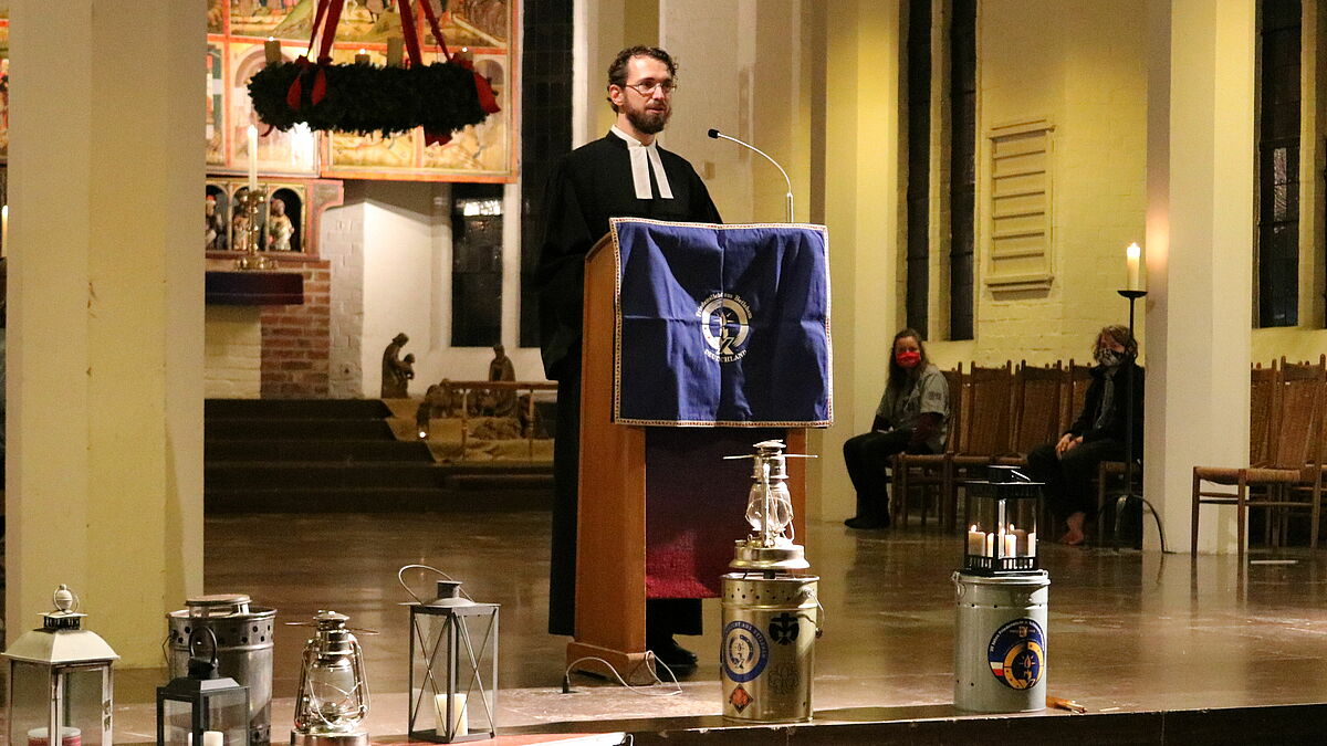 Christian Ehrens hält die Predigt beim Friedenslichtgottesdienst in Kiel, im Vordergrund die mitgebrachten Laternen der Pfadfinderstämme sowie die Behälter mit dem Friedenslicht aus Bethlehem.