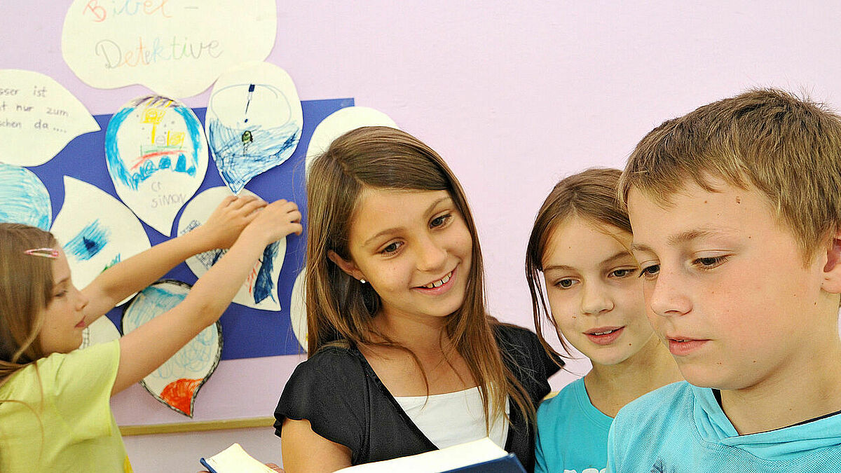 Kinder einer dritten Klasse schauen im Religionsunterricht gemeinsam in eine Bibel (Archiv).
