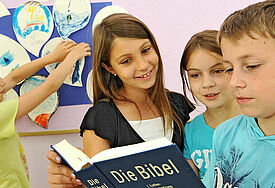 Kinder schauen gemeinsam in eine aufgeschlagene Bibel.
