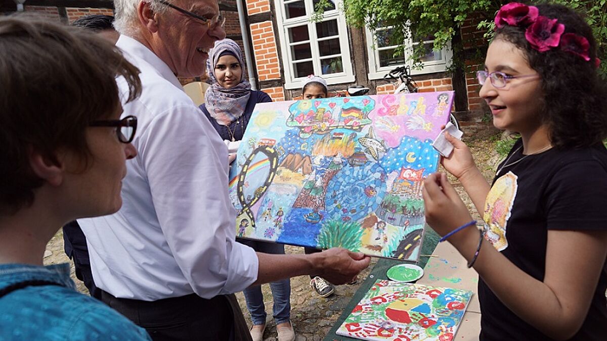 Die elfjährige Sabiha, die 2016 mit ihren Eltern auf der Flucht aus Syrien nach Mecklenburg kam, erläutert Landesbischof Gerhard Ulrich ein selbstgemaltes Bild. Es erzählt von den Stationen ihrer Flucht, von Ängsten, Hoffnungen und Träumen des Mädchens