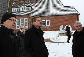 Ministerpräsident Daniel Günther (Mitte) und Bischof Gothart Magaard (links) auf dem Gelände der Neulandhalle, die die Nazis als "Anti-Kirche" konzipiert hatten