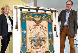Links steht die Archivleiterin, rechts der Propst in der Mitte die fast menschengroße Flagge, deren Farben wieder kräftig sind.