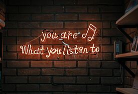 Rote Neon-Leuchtschrift auf Backsteinwand "You are what you listen to"