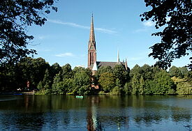 75. Jahrestag: St. Gertrud gedenkt Luftangriffen Kirche mit langem schlanken Turm am Kuhmühlenteich im Grünen bei Sonnenschein und blauem Himmel