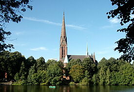 Kirche mit langem schlanken Turm am Kuhmühlenteich im Grünen bei Sonnenschein und blauem Himmel