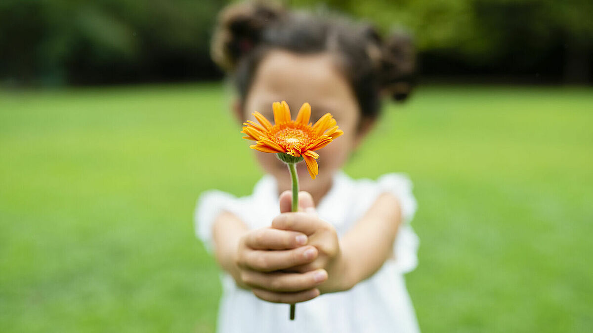 Mädchen streckt Blume Betrachter entgegen