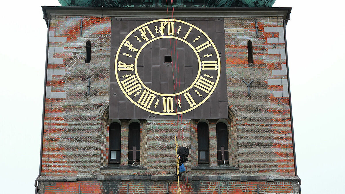 Kletterer Henrik Meger seilt sich vom St.-Jakobi-Kirchturm in Lübeck ab, um die drei verbliebenen Uhrzeiger in das Kirchturminnere zu bringen.