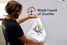 Eine Person hält eine Stofftasche mit dem Logo der Vollversammlung hoch