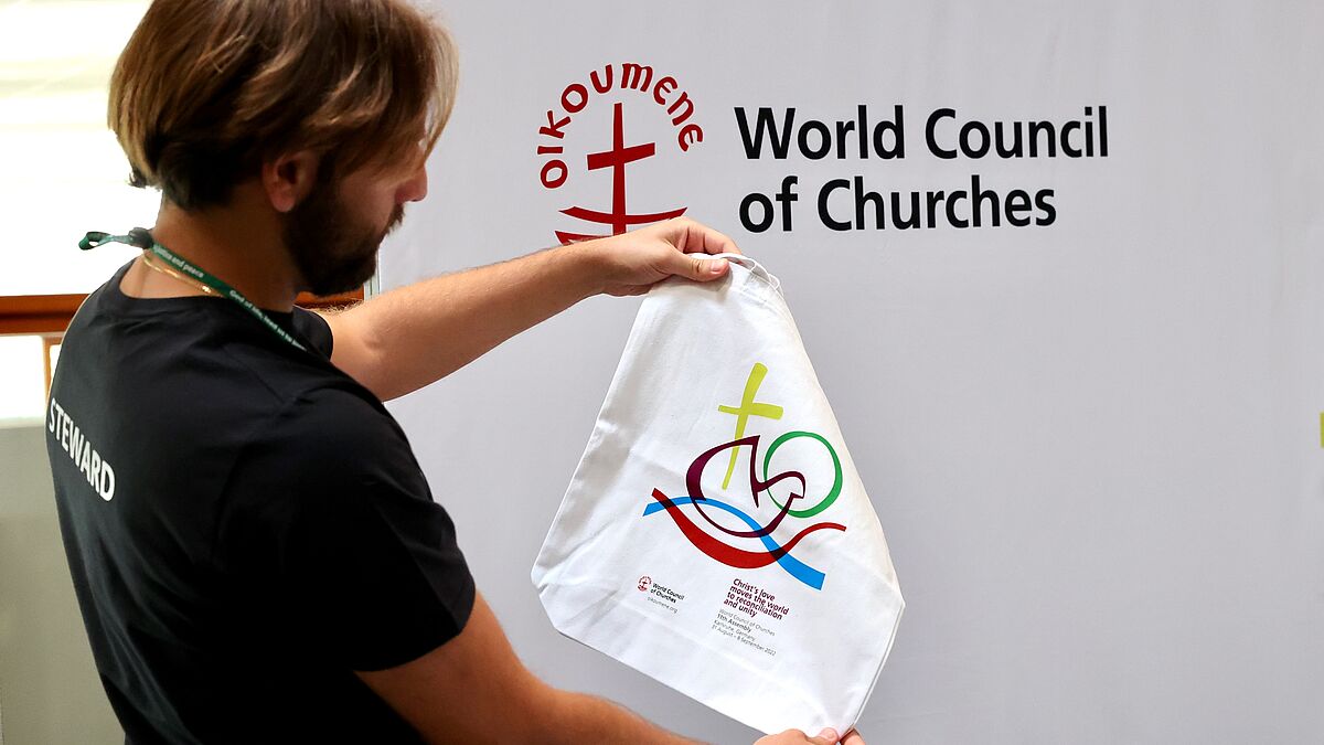 Eine Person hält eine Stofftasche mit dem Logo der Vollversammlung hoch