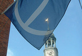 Mehr Übernachtungen im Seemannsheim Krayenkamp Flagge des Seemannsheims weht im Wind, dahinter sieht man die Spitze des Michels