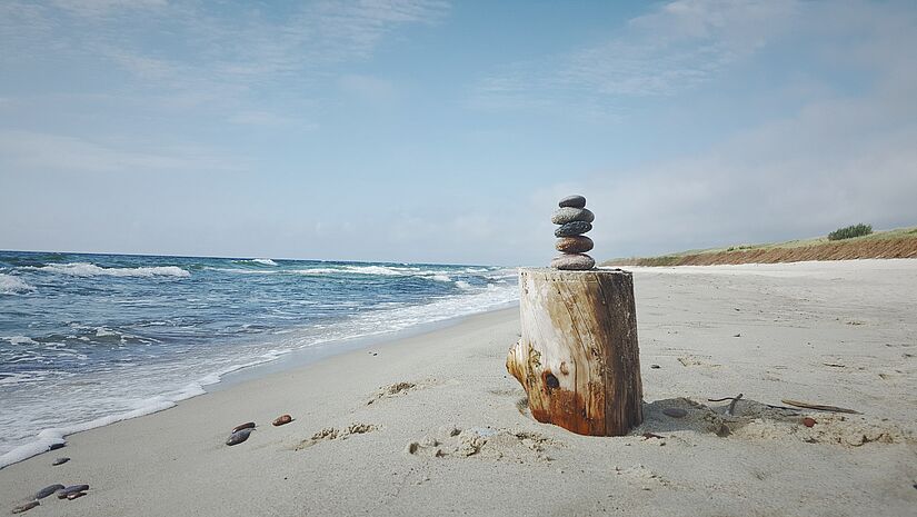Runde, flache Steine liegen gestapelt auf einen Holzstamm am Meer.