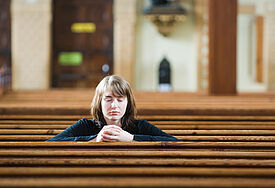 Eine Frau sitzt, in ihr Gebet vertieft, in einer Kirche (Symbolbild)