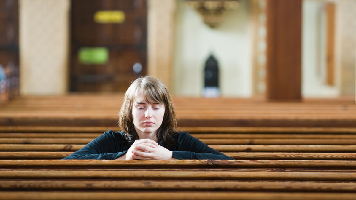 Eine Frau sitzt, in ihr Gebet vertieft, in einer Kirche (Symbolbild)