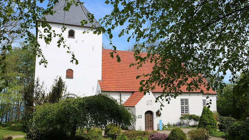 Eine kleine weiße Steinkirche aus romanischer Zeit mit Büschen und Bäumen 